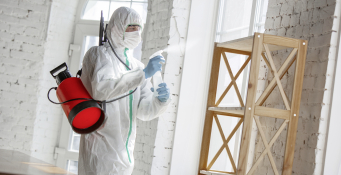 Coronavirus Pandemic. A disinfector in a protective suit and mask sprays disinfectants in the room. Protection of COVID-19 disease. Prevention of spreding pneumonia virus with surfaces we touch.